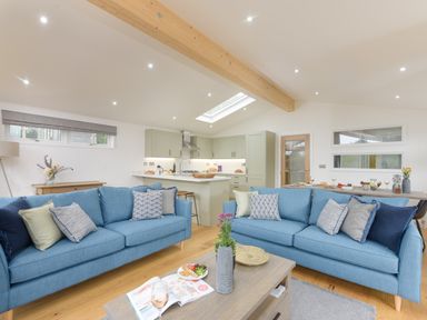An open plan living room and kitchen with two blue sofas and a wooden coffee table at 4 Valley View in Lanreath