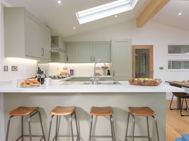 A kitchen with a white countertop island and four wooden stools at 4 Valley View in Lanreath