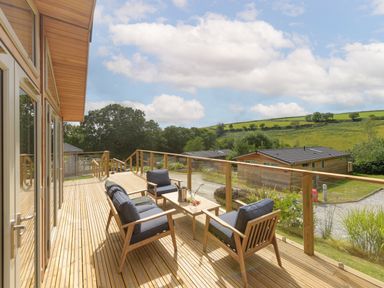 A wooden balcony with outdoor chairs and a table overlooking green hills at 4 Valley View in Lanreath