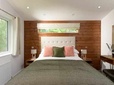 A bedroom with a bed with green and pink pillows a wooden feature wall and a window at 4 Valley View in Lanreath