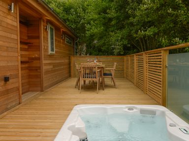 An outdoor wooden deck with a hot tub in the foreground and a dining table with chairs in the background at 4 Valley View in Lanreath