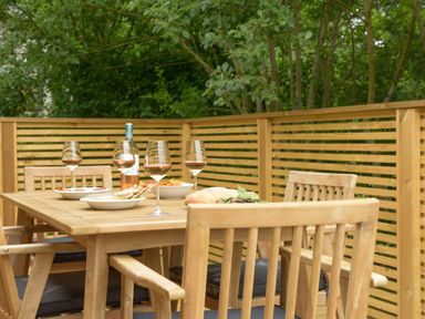 An outdoor wooden dining table set with glasses of wine plates of food and surrounded by wooden chairs on a deck at 4 Valley View in Lanreath