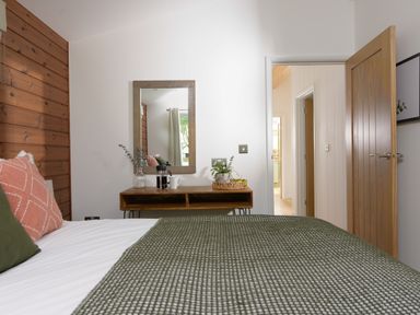 A bedroom with a bed featuring green and pink pillows wooden wall paneling a wooden table with a mirror and plants at 4 Valley View in Lanreath