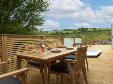 A wooden outdoor dining table set with four chairs and food with a scenic countryside view at 4 Valley View in Lanreath