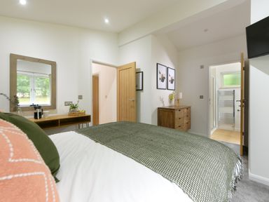 A bedroom with a bed a wooden dresser a mirror and an open door showing a bathroom at 4 Valley View Lanreath