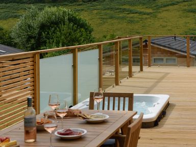 A wooden deck with a dining table set with wine glasses and plates and a hot tub at 4 Valley View in Lanreath