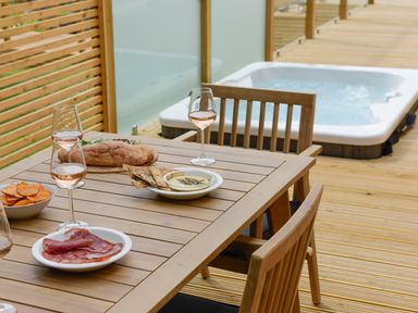 An outdoor wooden dining table with plates of food and glasses of wine near a hot tub on a wooden deck at 4 Valley View in Lanreath