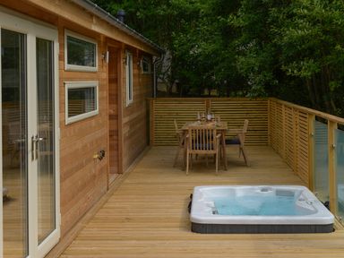 A wooden outdoor deck with a built in hot tub and a dining table with chairs at 4 Valley View in Lanreath