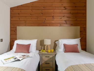 A bedroom with two single beds with white bedding and pink pillows a wooden headboard a wooden nightstand with a lamp two glasses of orange juice and two apples at 4 Valley View in Lanreath