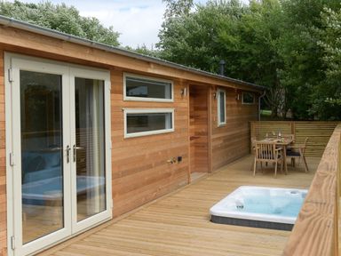 A wooden deck with a hot tub and outdoor dining table next to a wood-paneled building at 4 Valley View in Lanreath