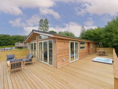 A wooden deck with outdoor seating and a hot tub attached to a wooden cabin at 4 Valley View in Lanreath