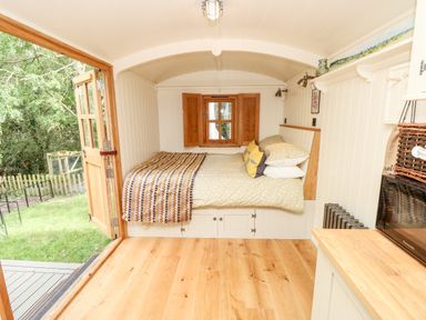 A small room with a bed under a window and wooden floor with open doors leading outside at The Happy Hut in Sopley near Christchurch