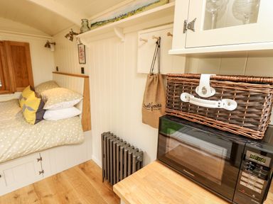 A small room with a bed with pillows a microwave on a wooden counter a wicker basket and a radiator at The Happy Hut in Sopley near Christchurch