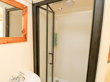 A bathroom with a glass shower enclosure a handheld and rain shower head a white sink with silver taps and a wooden framed mirror at The Happy Hut in Sopley near Christchurch