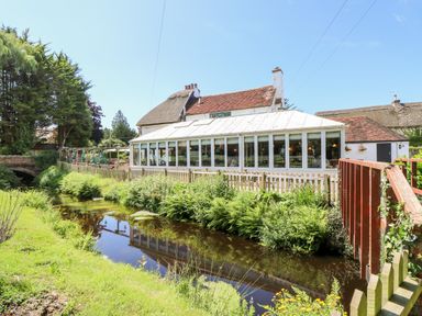 A building with a glass conservatory next to a small river and surrounded by greenery at The Happy Hut in Sopley near Christchurch