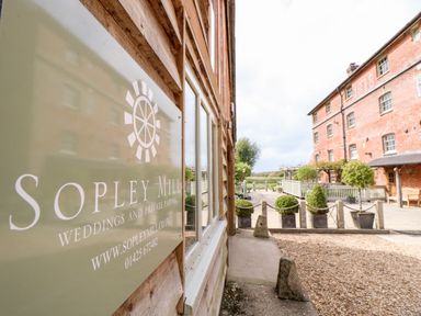 An exterior view of a building with a sign reading sopley mill weddings and private parties next to a paved area with potted plants and a brick building in the background at The Happy Hut in Sopley near Christchurch