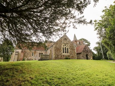 A stone church with a red tiled roof on a grassy slope with trees around at The Happy Hut in Sopley near Christchurch