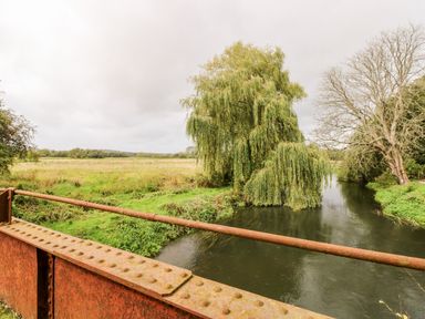 A view of a river with trees and grassy fields from a rusty metal bridge at The Happy Hut in Sopley near Christchurch