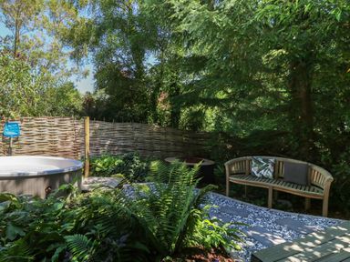 An outdoor garden area with a round hot tub wooden bench with cushions and a stone pathway at The Happy Hut in Sopley near Christchurch