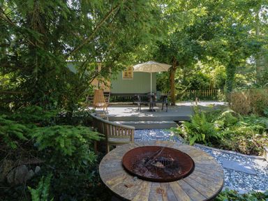 A garden area with a fire pit wooden chair and a green cabin with a patio umbrella at The Happy Hut in Sopley near Christchurch