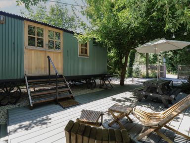 An outdoor deck with wooden chairs a picnic table with an umbrella and a green corrugated metal wagon at The Happy Hut in Sopley near Christchurch