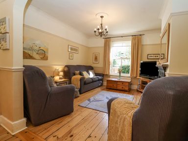 A living room with armchairs a sofa a wooden floor a rug a window with curtains and a television at Green Gate Cottage in Reydon near Southwold