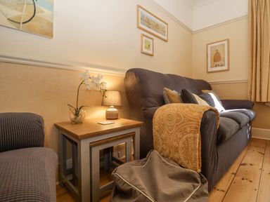 A living room with a sofa throw pillows side tables a lamp and wall art at Green Gate Cottage Reydon near Southwold