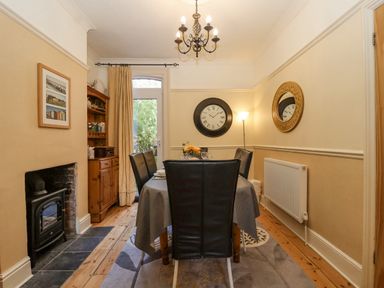 A dining room with a table and chairs a wall clock a mirror and a fireplace at Green Gate Cottage Reydon near Southwold