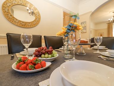 A dining table set with plates bowls glasses cutlery and bowls of strawberries and grapes at Green Gate Cottage Reydon near Southwold
