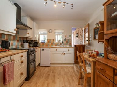 A kitchen with wooden cabinets a stove and a small dining table at Green Gate Cottage in Reydon near Southwold