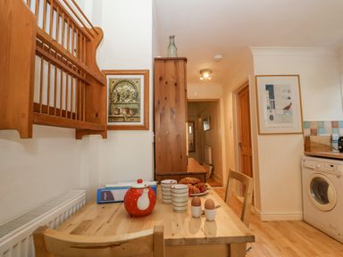 A kitchen with a wooden table set with a teapot cups eggs and croissants near a washing machine at Green Gate Cottage Reydon near Southwold