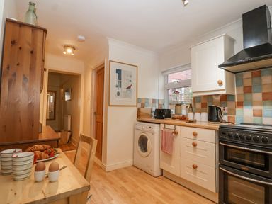 A kitchen with white cabinets a black oven a washing machine and a small wooden dining table with breakfast items at Green Gate Cottage Reydon near Southwold