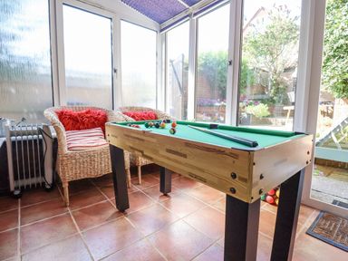 A sunroom with a small pool table two wicker chairs with cushions and a heater at Green Gate Cottage in Reydon near Southwold