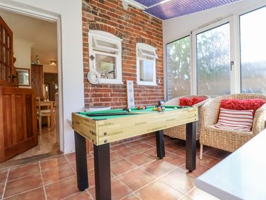 A room with a pool table wicker chairs and a brick wall at Green Gate Cottage Reydon near Southwold