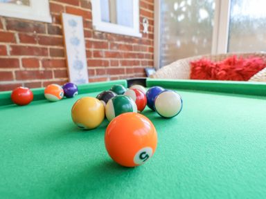A close up of billiard balls on a green pool table in a room with brick walls and a wicker chair at Green Gate Cottage in Reydon near Southwold