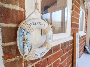 A welcome on board life ring hanging on a brick wall near a window at Green Gate Cottage in Reydon near Southwold