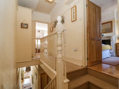 A stairway landing with beige carpet and white railing leading to two bedrooms at Green Gate Cottage in Reydon near Southwold