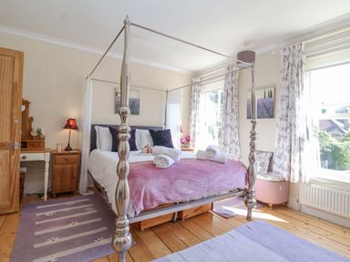 A bedroom with a four-poster bed with towels on the bed and floral curtains at Green Gate Cottage in Reydon near Southwold
