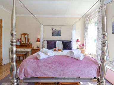 A bedroom with a four-poster bed with purple cushions and a pink blanket at Green Gate Cottage in Reydon near Southwold