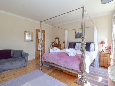 A bedroom with a four-poster bed sofa wooden floors and bedside tables at Green Gate Cottage in Reydon near Southwold