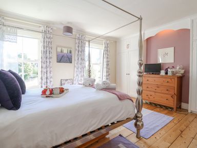 A bedroom with a four-poster bed wooden dresser and two windows with floral curtains at Green Gate Cottage Reydon near Southwold