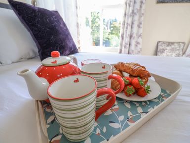A bedroom with a tray holding a teapot cups croissants and strawberries on a bed at Green Gate Cottage in Reydon near Southwold