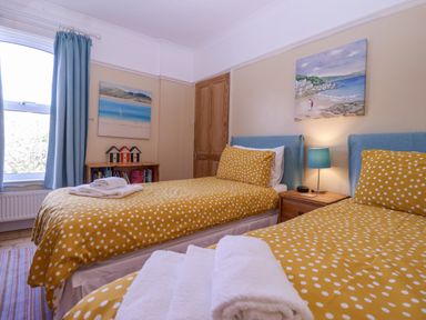 A bedroom with two single beds with yellow polka dot bedding a bedside table with a lamp and paintings on the wall at Green Gate Cottage Reydon near Southwold