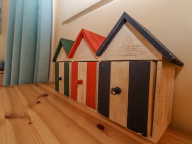 Three small wooden beach hut shaped cabinets with doors in green red and blue on a wooden surface at Green Gate Cottage in Reydon near Southwold