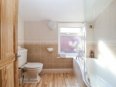 A bathroom with a toilet a bathtub a frosted window and wooden door at Green Gate Cottage in Reydon near Southwold
