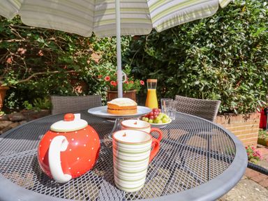 An outdoor metal table with teapot cups cake grapes orange juice under a patio umbrella at Green Gate Cottage in Reydon near Southwold