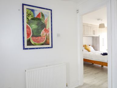 A hallway with a painting of watermelons on the wall and a bedroom with a bed and built-in wardrobe at Seaside Sanctuary in Trearddur Bay