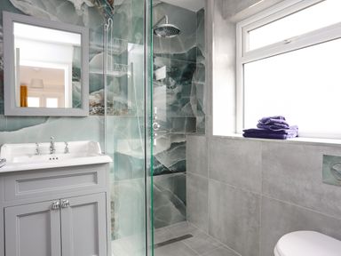 A bathroom with a sink cabinet mirror glass shower enclosure window and folded towels on the windowsill at Seaside Sanctuary in Trearddur Bay