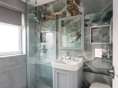 A bathroom with a glass shower enclosure a sink with a cabinet below and a mirror above at Seaside Sanctuary in Trearddur Bay
