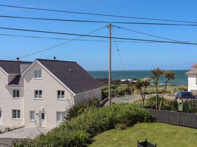 A white house near the ocean with green bushes and a lawn at Seaside Sanctuary in Trearddur Bay